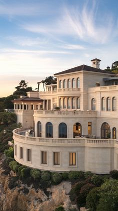 an aerial view of a large white house on the cliff with trees and bushes surrounding it