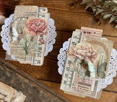 two pieces of paper with flowers on them sitting on top of a wooden table next to other items