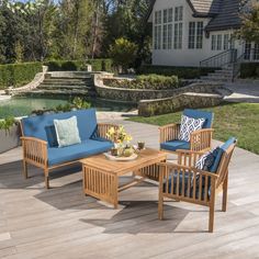 a wooden patio furniture set with blue cushions on a deck near a pond and house