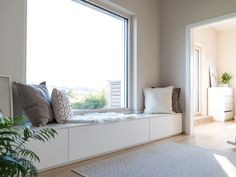 a window seat with pillows on it in front of a white rug and potted plant