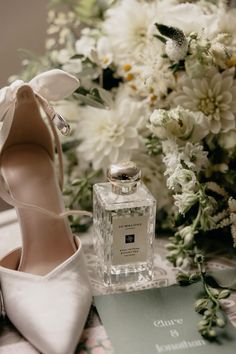 a pair of white high heels sitting next to a bottle of perfume and some flowers