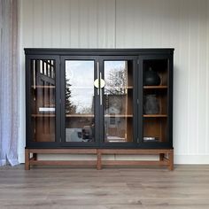 a black cabinet sitting on top of a hard wood floor next to a white wall