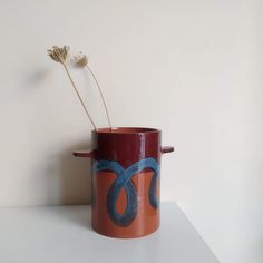 a red and blue vase with a flower in it on a white table next to a wall