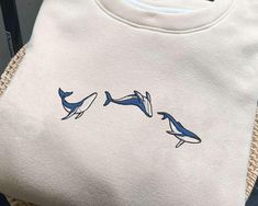 a white t - shirt with blue dolphins on it sitting next to a woven basket