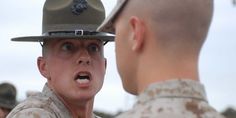 a man in uniform is talking to another man wearing a hat and looking at him