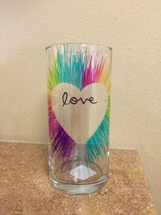 a shot glass with the word love painted on it and colored feathers in the shape of a heart