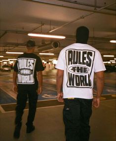 two men in black and white t - shirts walk through an empty parking garage area