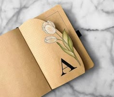 an open notebook with flowers on it and the letter a drawn in front of it