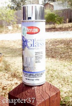 a can of glass paint sitting on top of a wooden post in front of a yard