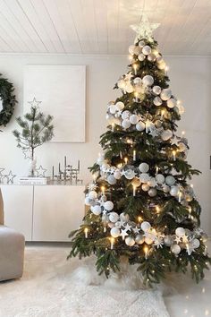 a decorated christmas tree in a living room with white and silver ornaments on the top