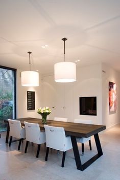 a dining room table with white chairs in front of a large window and a television mounted on the wall