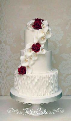 a three tiered wedding cake with red and white flowers