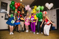 a group of people in costume posing for a photo with balloons and mario hats on