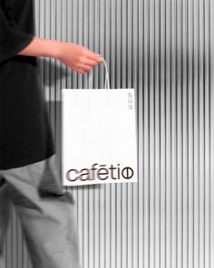 a person carrying a white shopping bag with the word cafeto on it's side