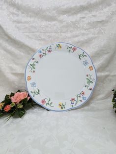 an empty plate sitting on top of a white table cloth next to some pink and yellow flowers