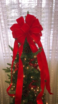 a christmas tree decorated with red ribbon and pine cones