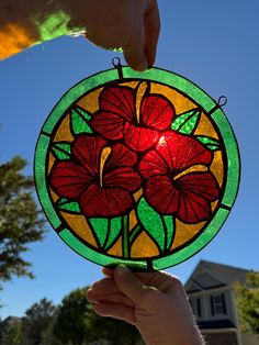 a hand holding a stained glass flower in front of a blue sky and green house