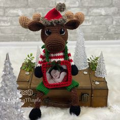 a crocheted moose with a christmas sweater and hat on sitting in a suitcase