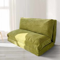 a green couch sitting on top of a hard wood floor next to a white wall