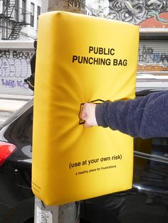 a person holding onto a yellow bag attached to a pole on the side of a street