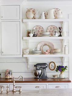 a kitchen with white cabinets and shelves filled with dishes on top of the countertop