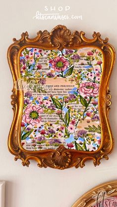 an ornate gold frame is hanging on the wall with flowers and words written below it