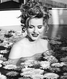 a black and white photo of a woman in a pool of water surrounded by daisies