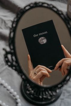 a person holding up a book in front of a mirror with the moon on it