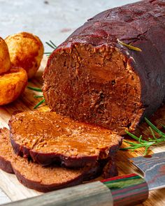 a sliced loaf of meat on a cutting board next to potato wedges and a knife