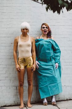 two women standing next to each other in front of a white brick wall wearing gold shorts