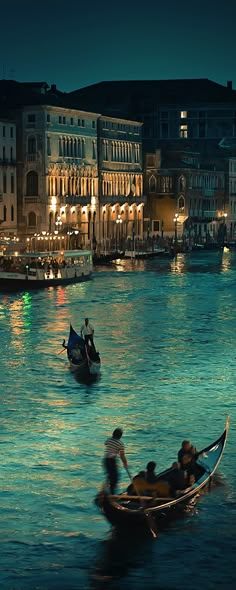 two gondolas in the water with people on them and buildings behind them at night