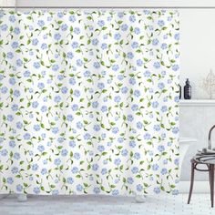 a shower curtain with blue flowers and green leaves on it in a white tiled bathroom