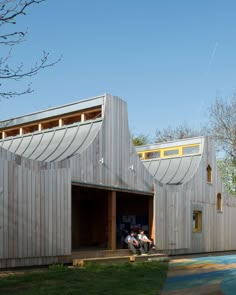 two people sitting on the steps outside of a wooden building with large windows and sloping roof