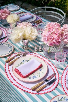 the table is set with plates, silverware and pink flowers