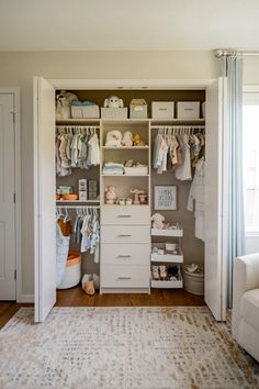 an organized closet with baby clothes and other items on shelves in the corner, along with a white chair