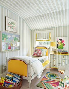 a bedroom with striped walls and yellow bedding, colorful rugs and pictures on the wall