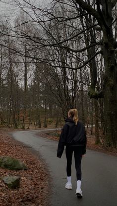 a woman walking down a path in the woods with trees and leaves on both sides