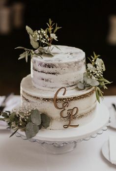 a three tiered wedding cake with greenery and initials on the top is sitting on a table