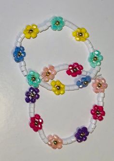 two bracelets with flowers and beads on white string, one is multicolored