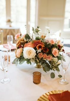 an arrangement of flowers and greenery on a white table cloth at a wedding reception