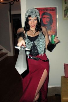 a woman dressed up in costume holding a can and knife while standing next to a couch