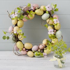 a wreath made out of eggs and flowers on a table next to a potted plant