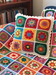 a crocheted granny blanket and pillow on top of a bed with bookshelves in the background