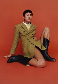 a woman sitting on the ground with her legs crossed wearing black boots and a yellow jacket