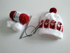 two knitted hats, yarn and needles on a white surface with one knitting needle