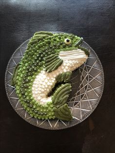 a fish made out of broccoli on top of a metal plate with white and green decorations