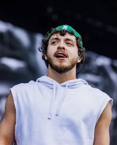 a man wearing a green bandanna standing in front of a large screen with his eyes closed