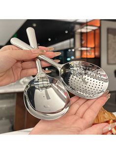 two hands are holding silver strainers in front of each other