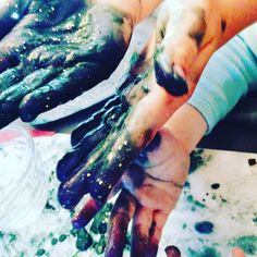 two people holding their hands covered in green and purple food dyes, while sitting at a table