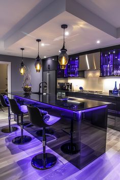 a kitchen with an island and purple lighting in the center is lit up by pendant lights that are hanging from the ceiling